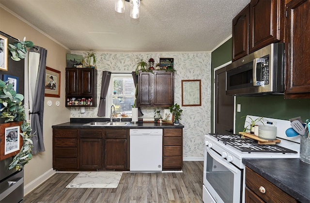 kitchen with white appliances, a sink, baseboards, ornamental molding, and wallpapered walls