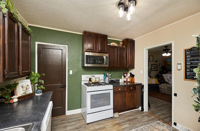 kitchen featuring white appliances, ornamental molding, light wood-type flooring, a textured ceiling, and dark countertops