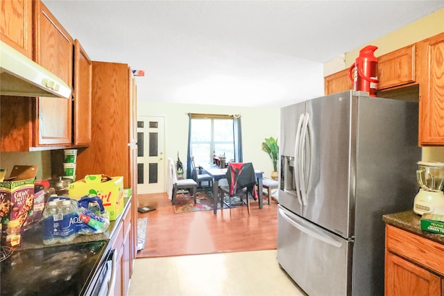 1424 Cleveland Ave, Des Moines, IA 50316 - kitchen featuring stainless steel refrigerator with ice dispenser, brown cabinetry, under cabinet range hood, light floors, and dark stone countertops