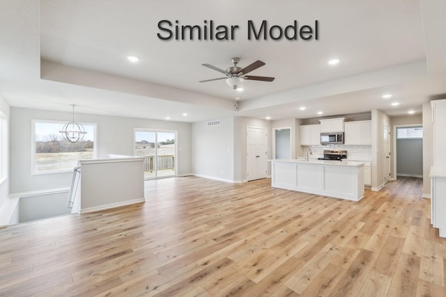 unfurnished living room featuring recessed lighting, light wood finished floors, a chandelier, ceiling fan, and a sink