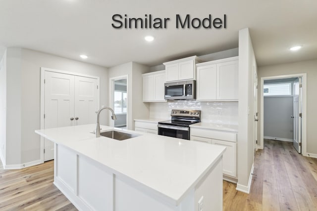 kitchen with stainless steel appliances, a sink, a center island with sink, light wood-style floors, and white cabinetry