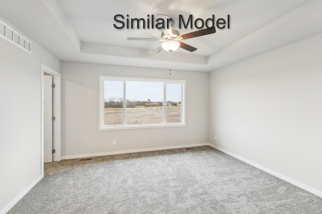 carpeted empty room featuring a raised ceiling, a ceiling fan, and baseboards
