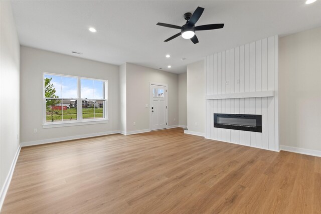 1998 S Warrior Ln, Waukee, IA 50263 - unfurnished living room with a large fireplace, light wood-style floors, ceiling fan, healthy amount of natural light, and recessed lighting