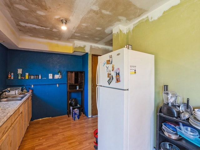 kitchen featuring freestanding refrigerator, a sink, light wood-type flooring, and light countertops