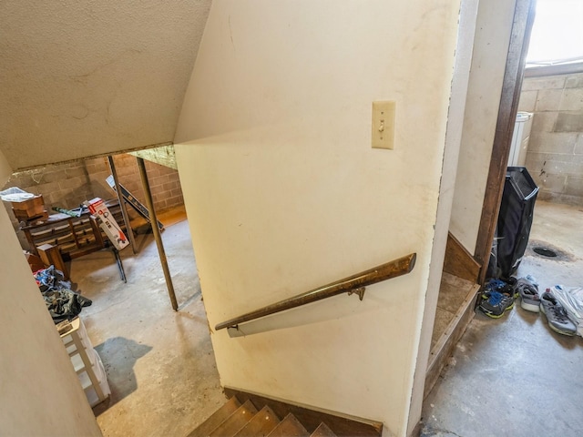 stairway featuring unfinished concrete flooring, concrete block wall, and lofted ceiling