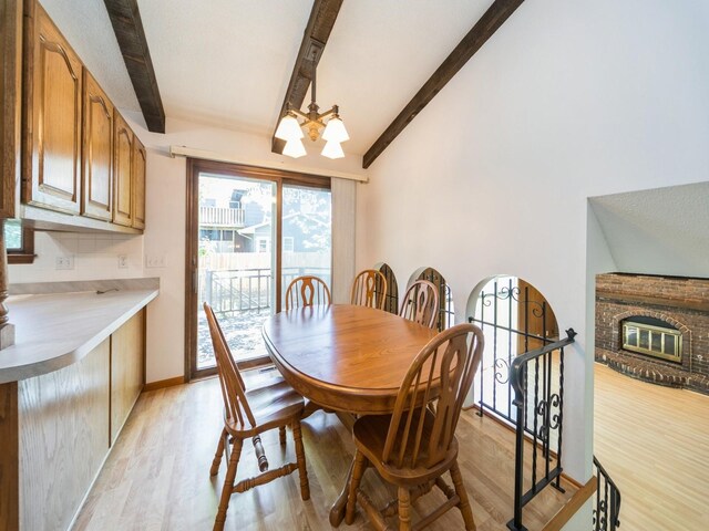 dining area featuring beamed ceiling, a chandelier, light wood-style flooring, and a fireplace