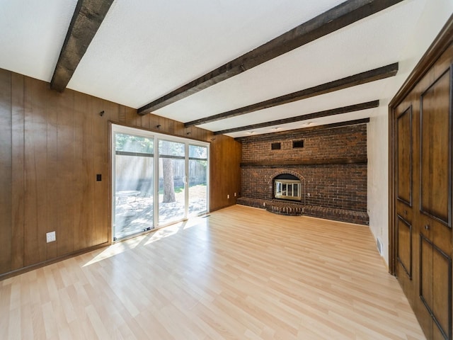 unfurnished living room featuring light wood-type flooring, wood walls, beamed ceiling, and a fireplace