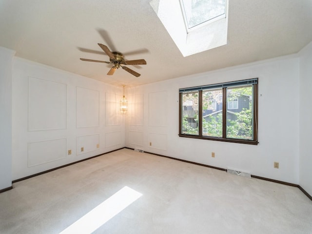 carpeted empty room featuring a skylight, ceiling fan, and baseboards