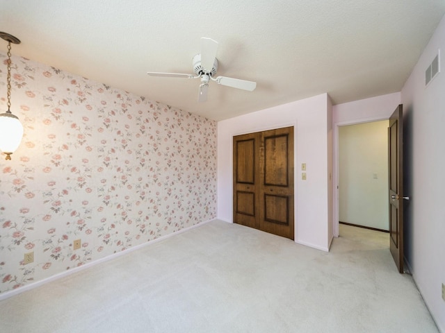unfurnished bedroom with light colored carpet, wallpapered walls, a ceiling fan, and baseboards