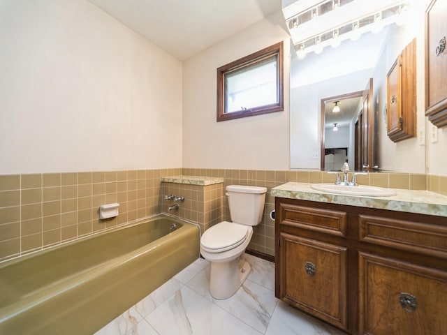 full bath featuring toilet, a bath, vanity, tile walls, and wainscoting