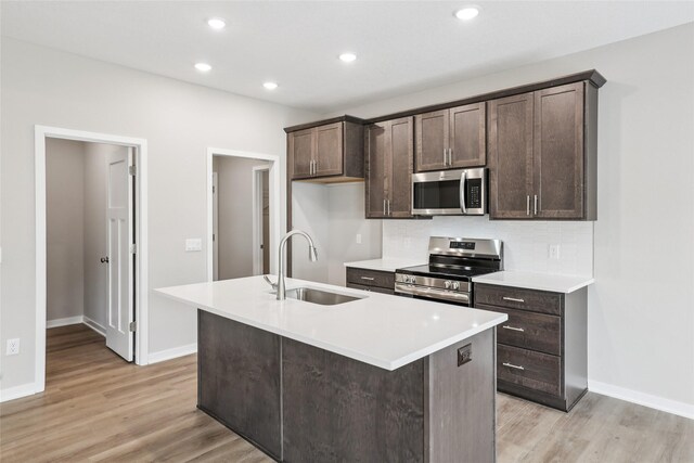 2331 N 8th Ave E, Newton, IA 50208 - kitchen with appliances with stainless steel finishes, a sink, dark brown cabinetry, light wood-style flooring, and an island with sink