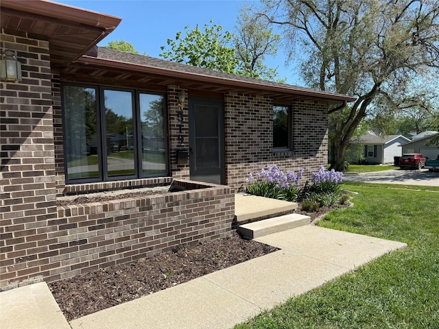 view of exterior entry featuring a yard and brick siding