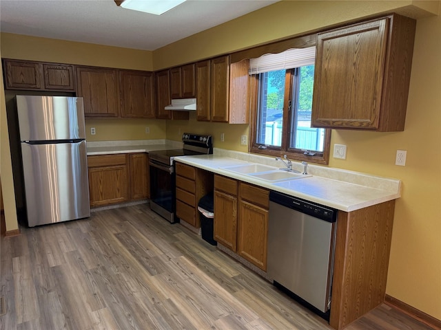 kitchen featuring appliances with stainless steel finishes, a sink, light wood-type flooring, range hood, and light countertops