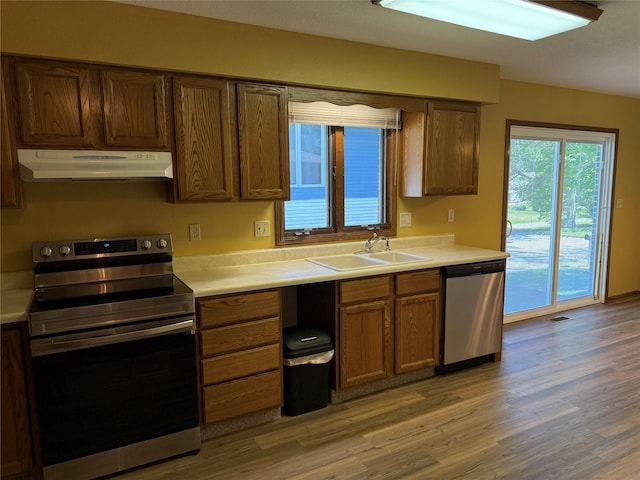 kitchen featuring under cabinet range hood, stainless steel appliances, light wood finished floors, and light countertops