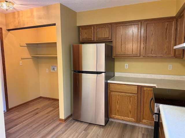kitchen with appliances with stainless steel finishes, light wood-type flooring, brown cabinetry, light countertops, and a textured ceiling
