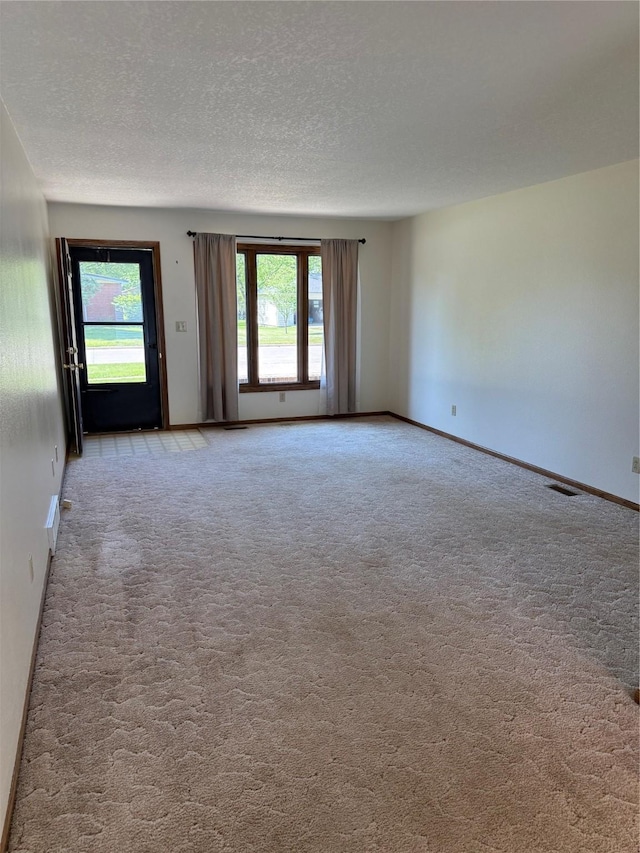 unfurnished room with carpet floors, healthy amount of natural light, a textured ceiling, and baseboards