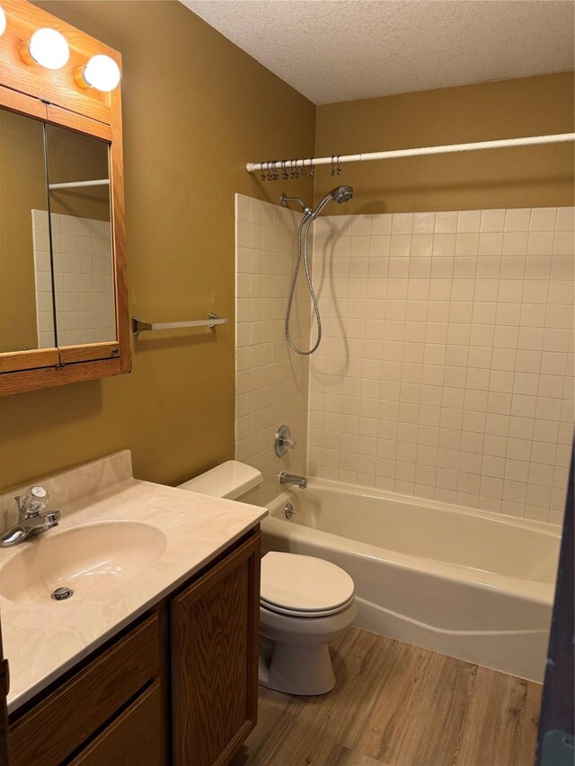 bathroom featuring wood finished floors, a textured ceiling, toilet, vanity, and bathing tub / shower combination