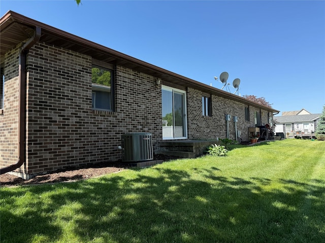 rear view of property with cooling unit, brick siding, and a yard