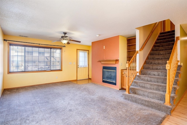 1509 SE Delaware Ave Unit 10, Ankeny, IA 50021 - unfurnished living room featuring a glass covered fireplace, stairs, baseboards, ceiling fan, and carpet flooring