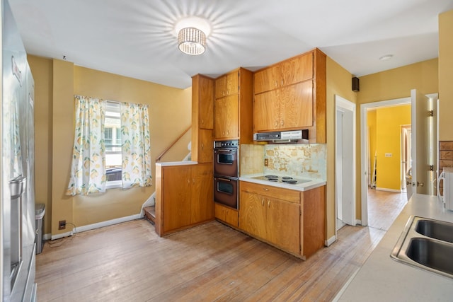 910 Washington St, Eldora, IA 50627 - kitchen with backsplash, electric stovetop, light countertops, light wood finished floors, and under cabinet range hood