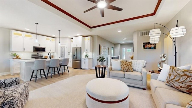 living room featuring a tray ceiling, ceiling fan, recessed lighting, light wood-style flooring, and ornamental molding