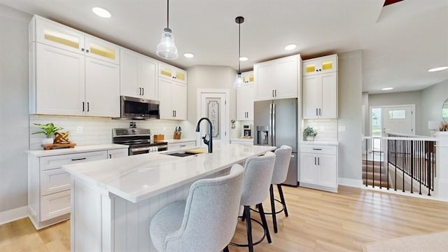kitchen with appliances with stainless steel finishes, a sink, a center island with sink, light wood-style flooring, and a breakfast bar