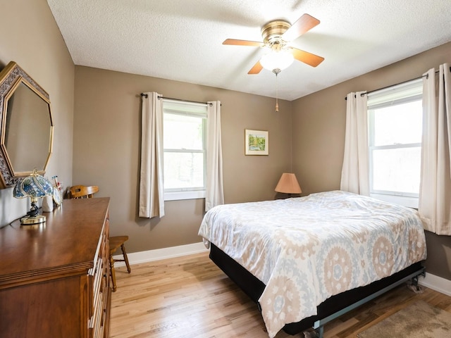 bedroom featuring multiple windows, baseboards, light wood-style floors, a textured ceiling, and a ceiling fan