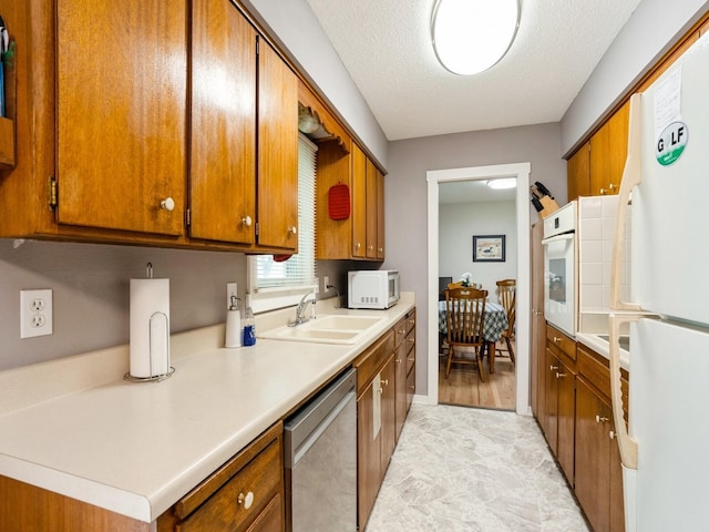 kitchen featuring white appliances, a sink, brown cabinetry, light countertops, and a textured ceiling