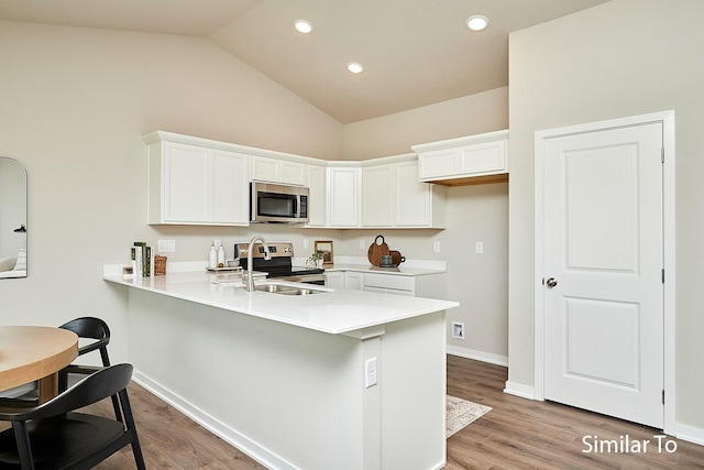 5560 165th St, Urbandale, IA 50323 - kitchen featuring appliances with stainless steel finishes, a peninsula, a sink, white cabinetry, and vaulted ceiling