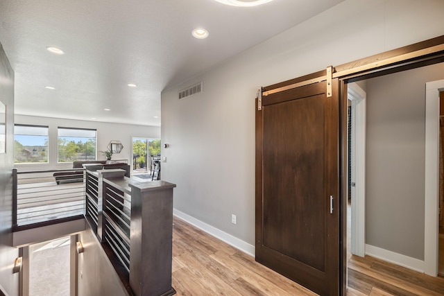 hallway featuring light wood-style flooring, recessed lighting, baseboards, and a barn door