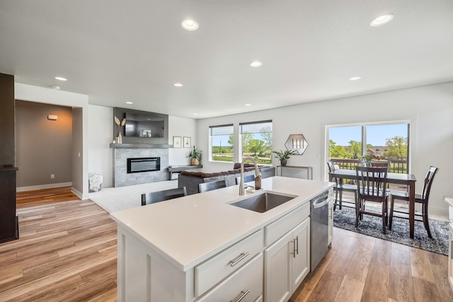 kitchen featuring a sink, stainless steel dishwasher, light wood-style floors, a glass covered fireplace, and recessed lighting