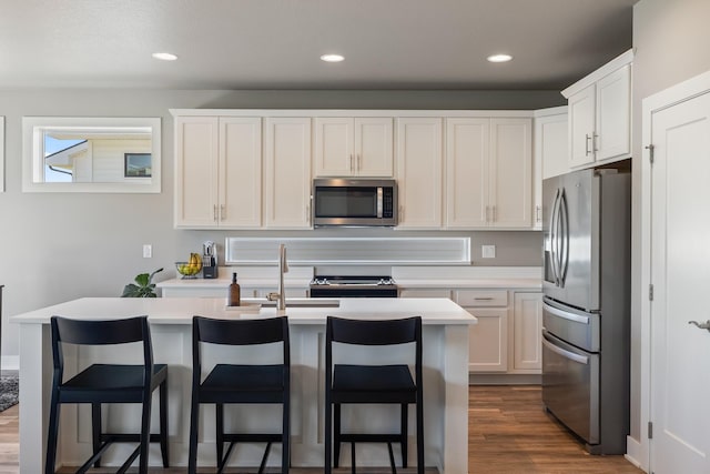 kitchen featuring appliances with stainless steel finishes, a sink, light countertops, dark wood-type flooring, and an island with sink