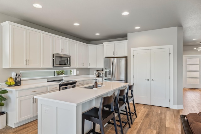 kitchen with stainless steel appliances, a sink, light wood finished floors, white cabinets, and recessed lighting