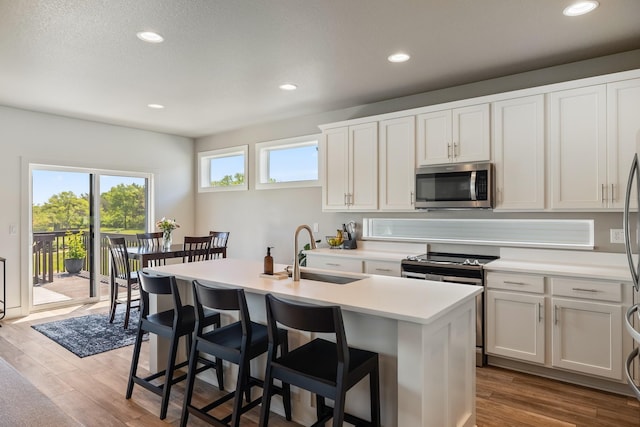 kitchen with stainless steel appliances, a sink, wood finished floors, light countertops, and a center island with sink