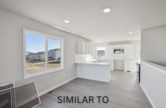 928 Spruce Ave, Norwalk, IA 50211 - kitchen with stainless steel microwave, a peninsula, white cabinetry, light wood-style floors, and decorative backsplash