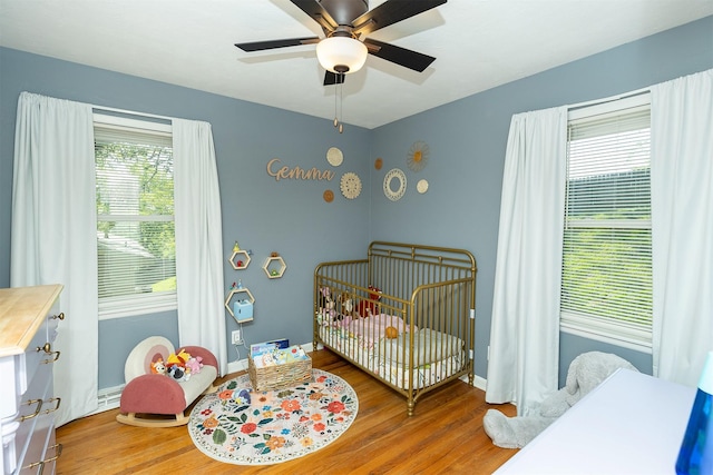 bedroom featuring a crib, wood finished floors, ceiling fan, and baseboards