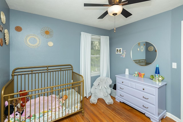 bedroom with wood finished floors, a crib, and a ceiling fan