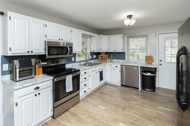 kitchen featuring appliances with stainless steel finishes, white cabinets, light wood-style flooring, and a sink