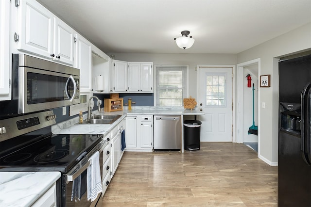 kitchen with appliances with stainless steel finishes, a sink, white cabinetry, and light wood finished floors