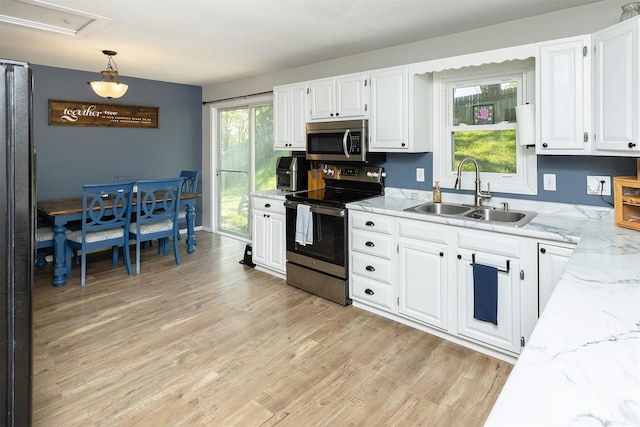 kitchen with appliances with stainless steel finishes, a sink, white cabinetry, light stone counters, and light wood-style flooring