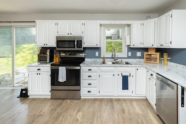 kitchen featuring stainless steel appliances, a sink, white cabinetry, light stone countertops, and light wood-style flooring