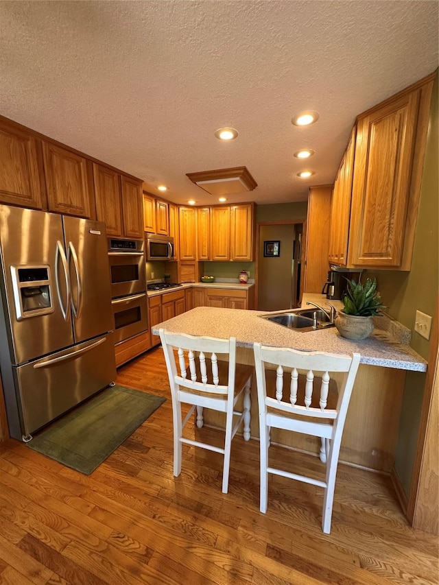 711 E Madison St, Winterset, IA 50273 - kitchen with stainless steel appliances, a peninsula, a textured ceiling, wood finished floors, and brown cabinetry