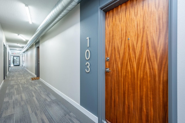 hall with baseboards and dark carpet