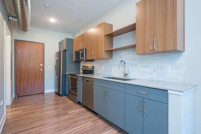 kitchen with stainless steel appliances, a sink, open shelves, light countertops, and light wood-style flooring