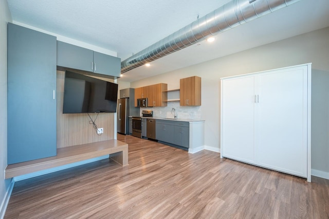 kitchen featuring stainless steel appliances, light wood-style flooring, light countertops, open shelves, and a sink