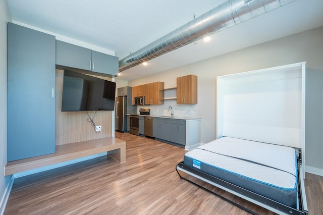 bedroom featuring freestanding refrigerator, light wood-style floors, a sink, and baseboards