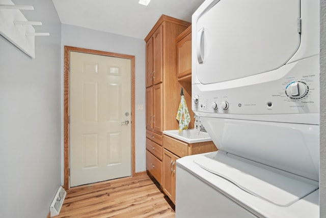 laundry room with estacked washer and dryer, cabinet space, and light wood-style flooring