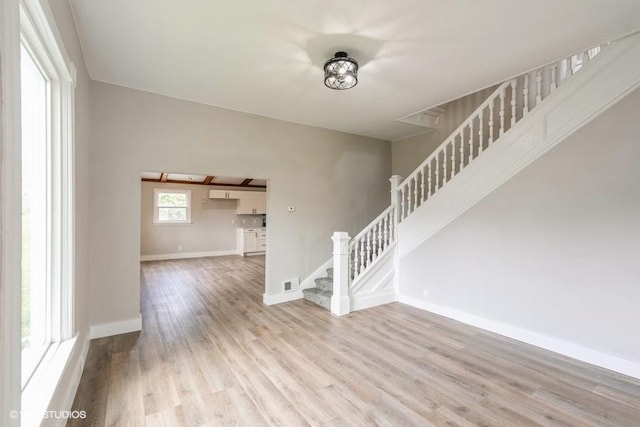 unfurnished living room with stairs, light wood-style floors, and baseboards