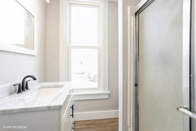 full bathroom with wood finished floors, vanity, a shower with door, and baseboards