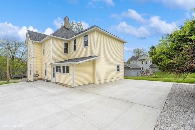 rear view of house with a chimney, driveway, and a patio area